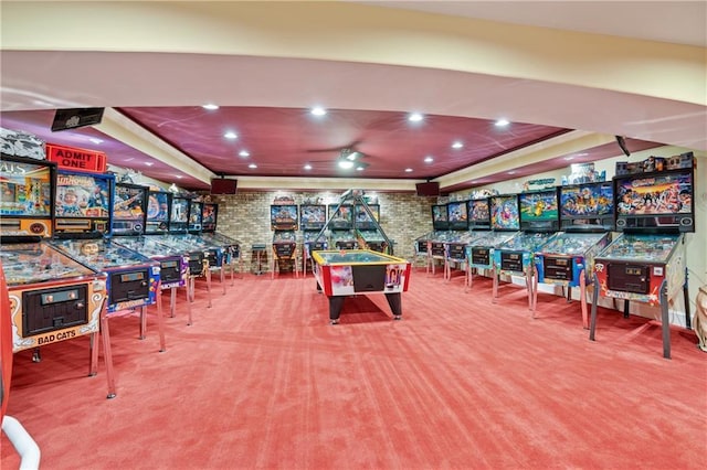 game room featuring a tray ceiling, carpet floors, and brick wall