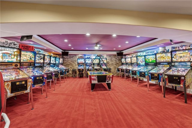 game room with brick wall, carpet, ceiling fan, and a tray ceiling