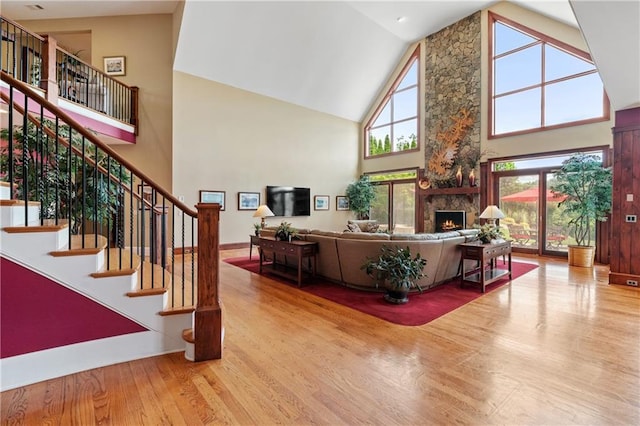 living room featuring a stone fireplace, high vaulted ceiling, and light wood-type flooring