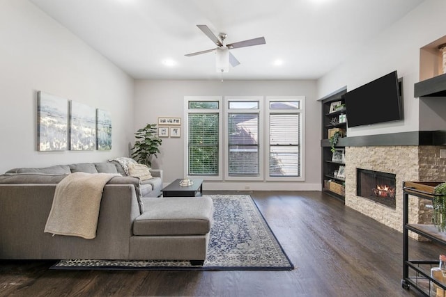 living room featuring dark hardwood / wood-style floors, ceiling fan, and a stone fireplace