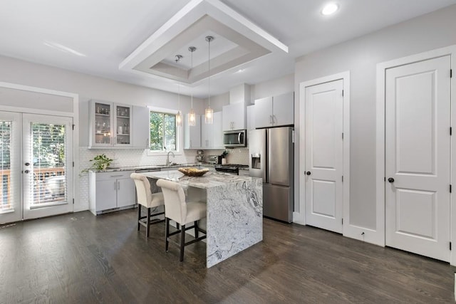 kitchen with stainless steel appliances, a kitchen island, dark hardwood / wood-style flooring, decorative light fixtures, and white cabinets