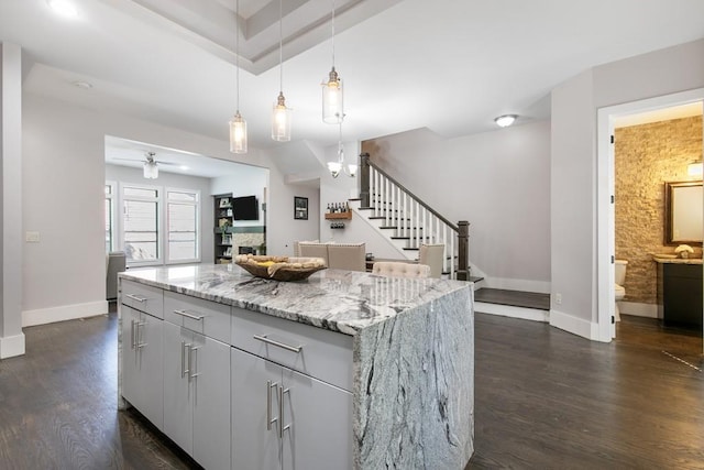 kitchen featuring light stone countertops, gray cabinetry, decorative light fixtures, a center island, and dark hardwood / wood-style floors