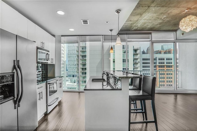 44 Peachtree Pl NE Unit 1929, Atlanta, GA 30309 - kitchen with appliances with stainless steel finishes, a sink, dark wood-style floors, white cabinets, and a kitchen bar