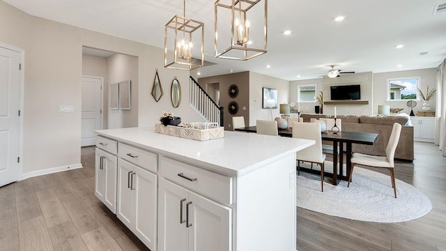 kitchen with wood finished floors, white cabinets, ceiling fan, a center island, and visible vents