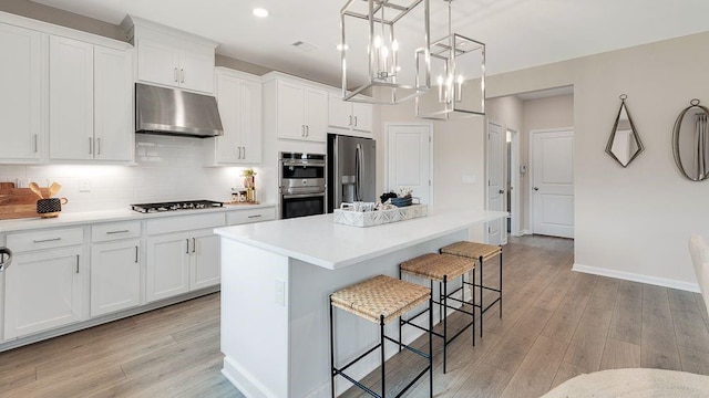 kitchen with stainless steel appliances, a center island, light wood finished floors, and under cabinet range hood