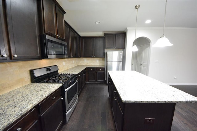 kitchen featuring appliances with stainless steel finishes, ornamental molding, arched walkways, a center island, and light stone countertops