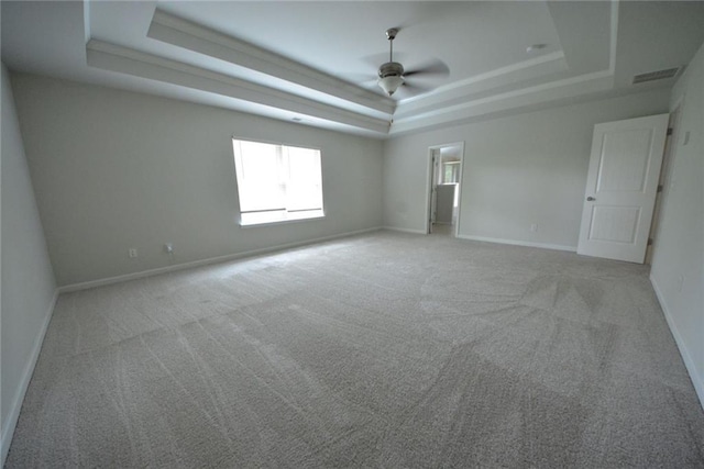 empty room featuring a tray ceiling, light colored carpet, a ceiling fan, and baseboards