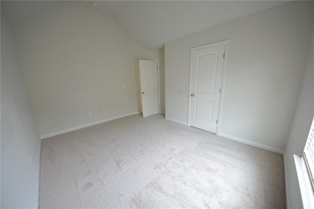 unfurnished bedroom featuring light carpet, lofted ceiling, and baseboards