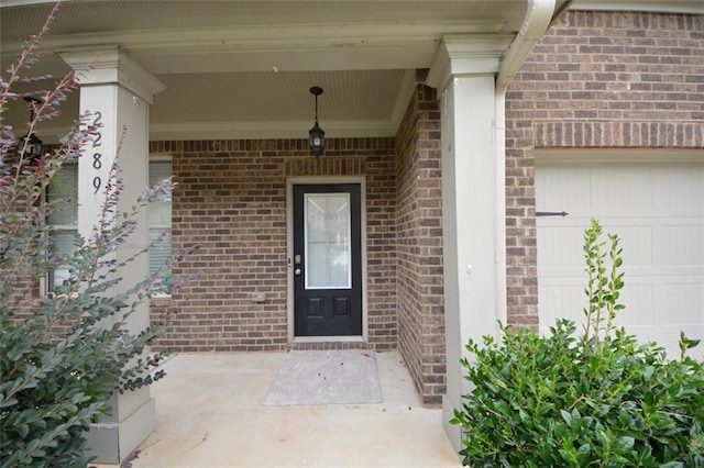 view of exterior entry with an attached garage, brick siding, and a porch