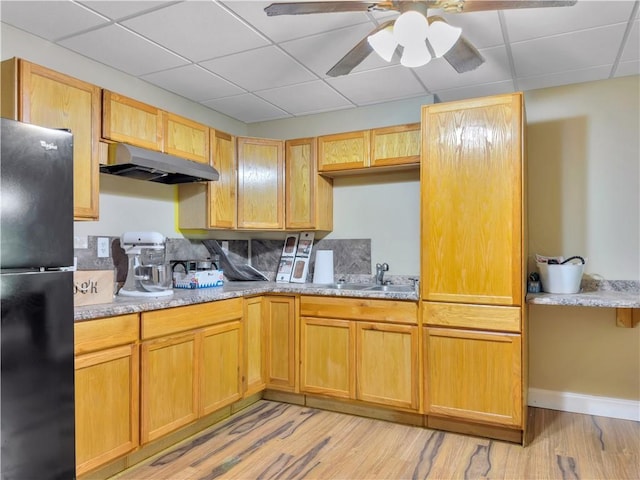 kitchen featuring light stone countertops, black fridge, and light wood-type flooring