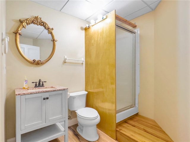 bathroom with wood-type flooring, vanity, toilet, and a drop ceiling