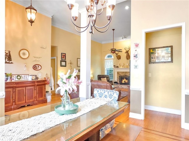 dining room featuring ornate columns, a brick fireplace, crown molding, light hardwood / wood-style floors, and ceiling fan with notable chandelier