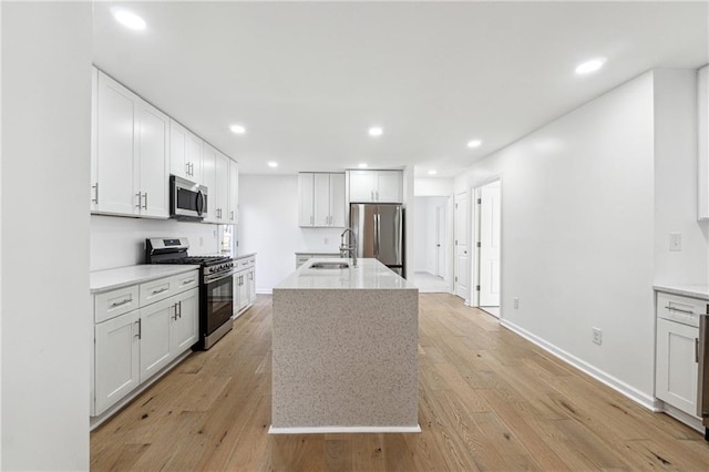 kitchen with a kitchen island with sink, light wood-type flooring, white cabinets, and appliances with stainless steel finishes