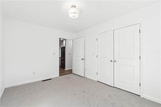 unfurnished bedroom featuring black fridge, light carpet, and a closet