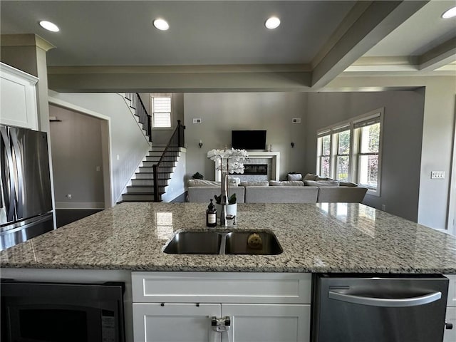 2657 Gray Mill Way, Loganville, GA 30052 - kitchen featuring a glass covered fireplace, an island with sink, appliances with stainless steel finishes, white cabinets, and open floor plan