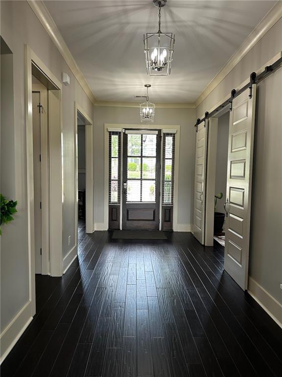 2657 Gray Mill Way, Loganville, GA 30052 - foyer featuring a barn door, baseboards, a chandelier, ornamental molding, and dark wood-type flooring