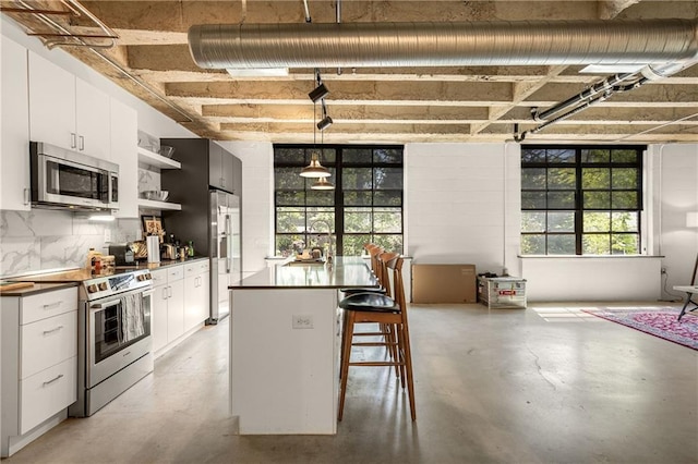 kitchen featuring white cabinets, open shelves, dark countertops, appliances with stainless steel finishes, and finished concrete flooring