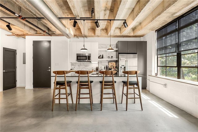 kitchen with concrete floors, a kitchen breakfast bar, backsplash, decorative light fixtures, and stainless steel appliances