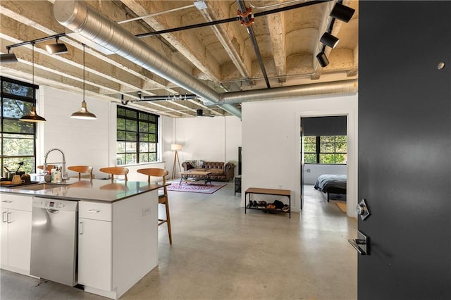 kitchen featuring hanging light fixtures, white cabinets, a sink, finished concrete flooring, and stainless steel dishwasher