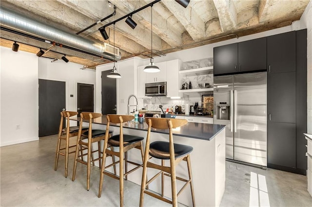 kitchen featuring dark cabinets, concrete floors, open shelves, a center island with sink, and stainless steel appliances