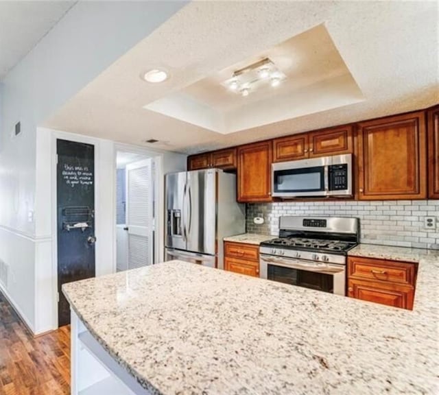 kitchen with stainless steel appliances, light hardwood / wood-style floors, a raised ceiling, and light stone countertops