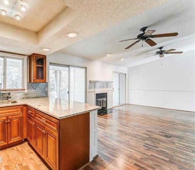 kitchen with light hardwood / wood-style floors, decorative backsplash, a textured ceiling, a tray ceiling, and light stone countertops