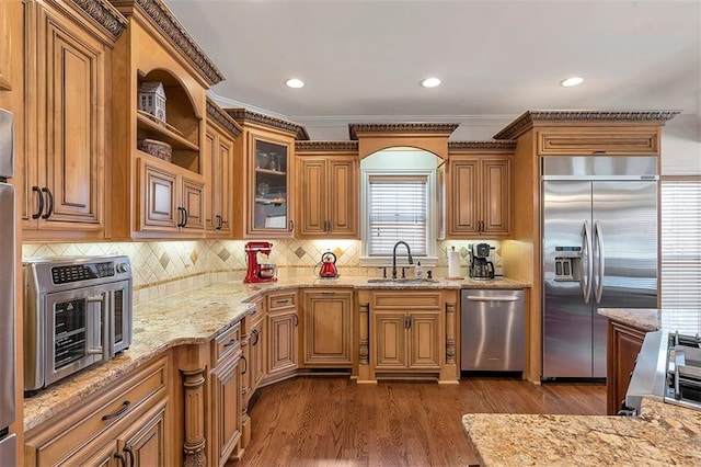 kitchen with light stone counters, a sink, stainless steel appliances, dark wood-type flooring, and backsplash