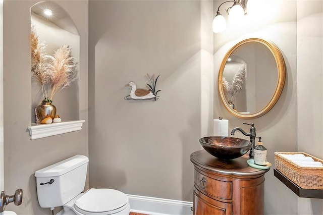 half bathroom featuring vanity, toilet, and baseboards