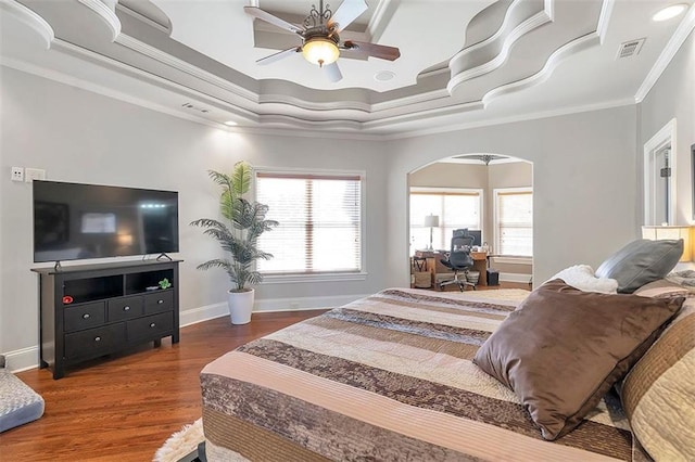 bedroom with crown molding, baseboards, a tray ceiling, wood finished floors, and arched walkways