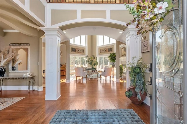 entryway featuring arched walkways, wood finished floors, ornate columns, and a towering ceiling