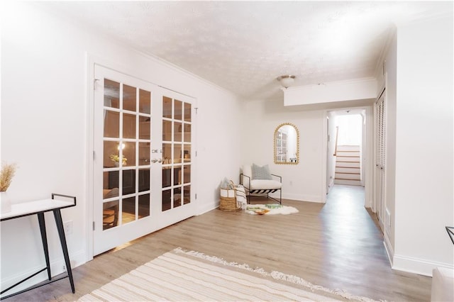 living area with ornamental molding, french doors, a textured ceiling, and light wood-type flooring