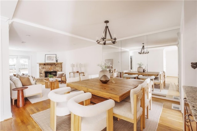 dining room with a notable chandelier, a stone fireplace, and light hardwood / wood-style flooring