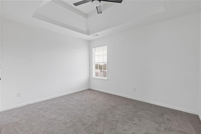 empty room with a tray ceiling, ceiling fan, and carpet