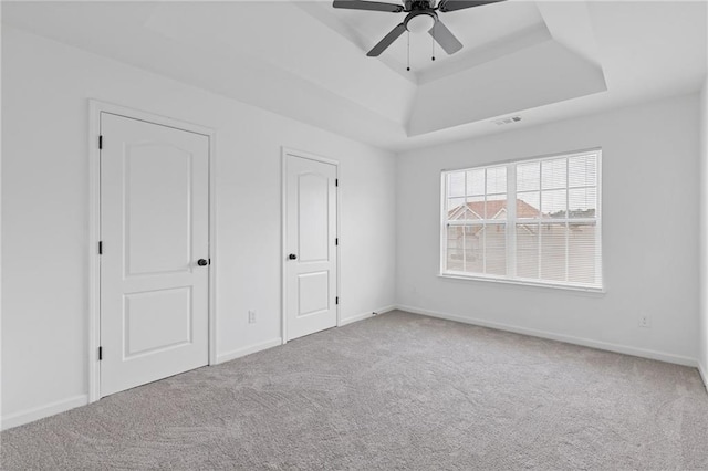 unfurnished bedroom with a raised ceiling, light colored carpet, and ceiling fan