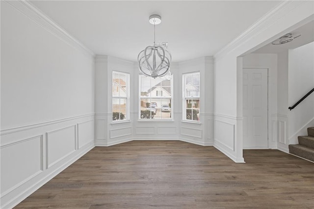 unfurnished dining area featuring wood-type flooring, plenty of natural light, ornamental molding, and a notable chandelier