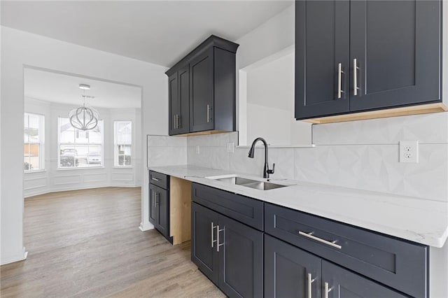 kitchen featuring pendant lighting, sink, backsplash, light stone countertops, and light wood-type flooring