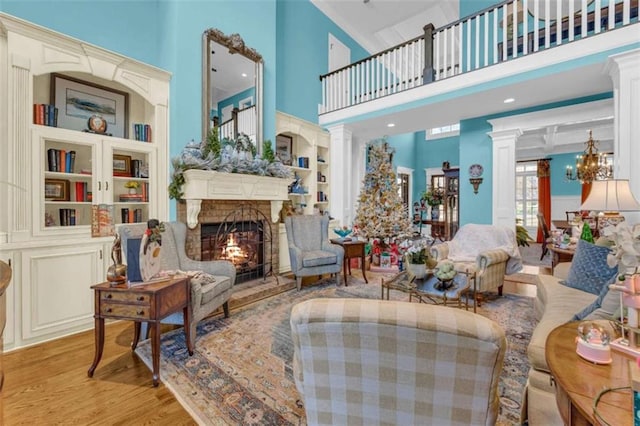 living room with a towering ceiling, decorative columns, an inviting chandelier, and light hardwood / wood-style floors