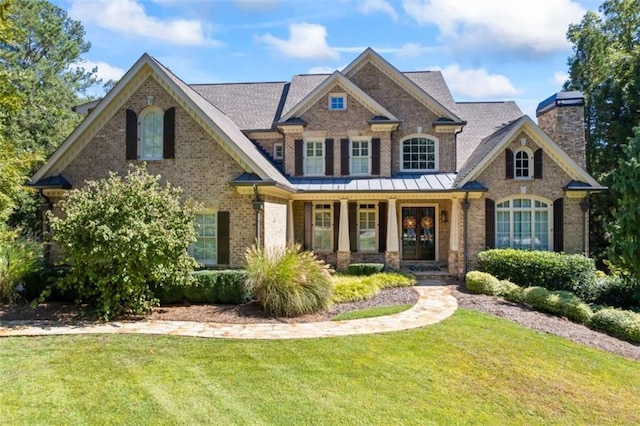 craftsman-style home with a porch, brick siding, a chimney, and a front lawn