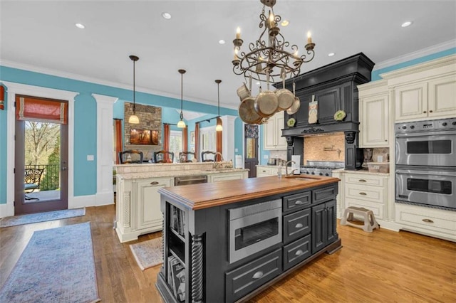 kitchen featuring wooden counters, tasteful backsplash, stainless steel appliances, a center island with sink, and hanging light fixtures