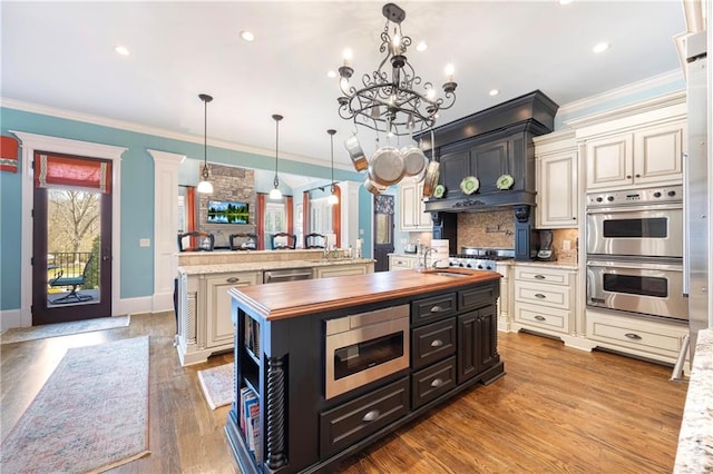 kitchen with a spacious island, crown molding, butcher block counters, appliances with stainless steel finishes, and cream cabinets