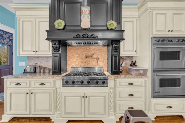 kitchen with cream cabinetry, decorative backsplash, stainless steel appliances, and premium range hood