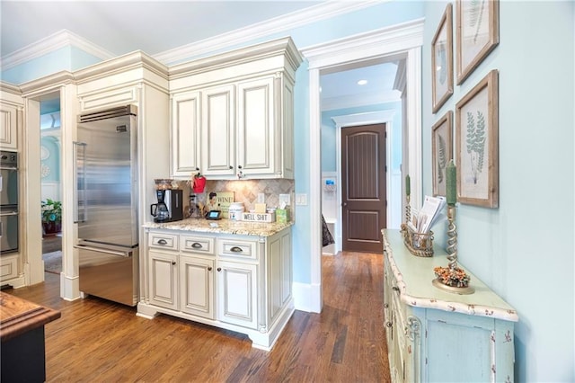 kitchen with dark wood-style flooring, ornamental molding, decorative backsplash, built in refrigerator, and cream cabinets