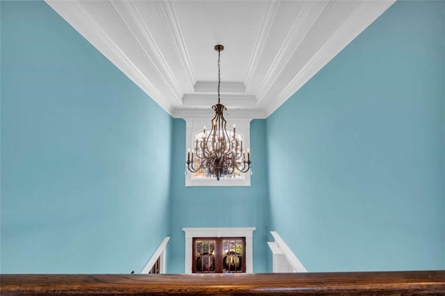 stairs with a tray ceiling, an inviting chandelier, and crown molding