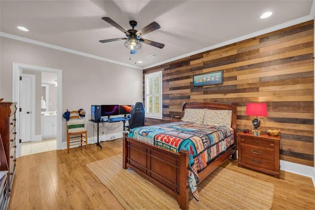 bedroom with ensuite bath, ceiling fan, crown molding, wooden walls, and light hardwood / wood-style flooring