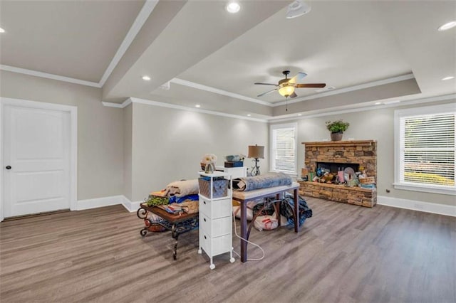 bedroom featuring hardwood / wood-style flooring, crown molding, a tray ceiling, and a stone fireplace