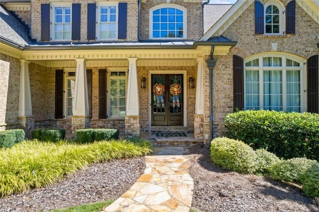 doorway to property featuring french doors, covered porch, and roof with shingles