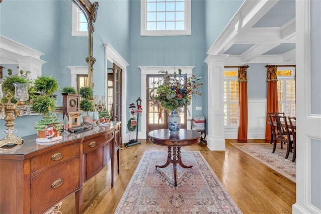 foyer featuring beamed ceiling, ornate columns, light wood-type flooring, and coffered ceiling