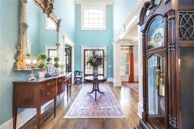 foyer entrance featuring baseboards, wood finished floors, a towering ceiling, and ornate columns