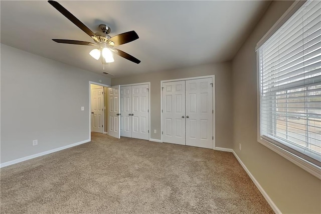 unfurnished bedroom featuring ceiling fan, multiple closets, and carpet flooring