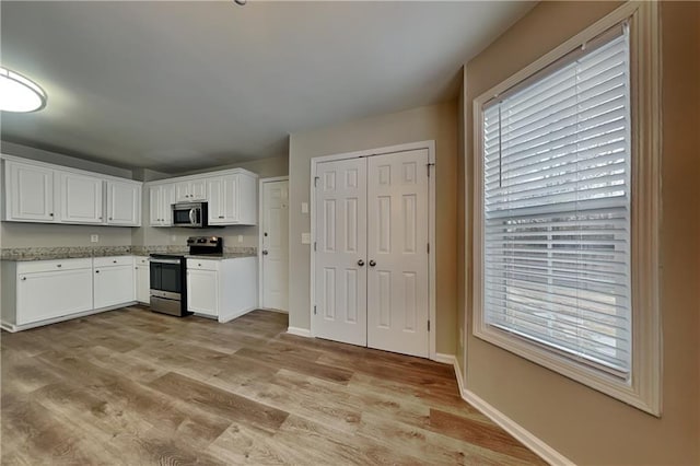 kitchen with light wood-type flooring, light stone countertops, white cabinets, and appliances with stainless steel finishes